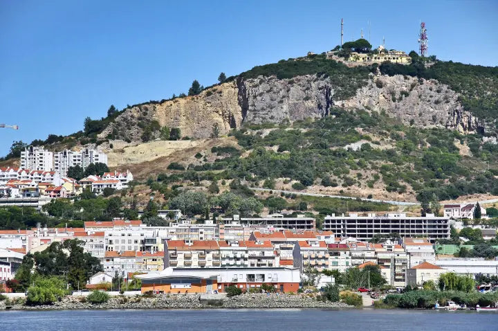 Vila Franca de Xira junto al río se extiende hacia una colina verde con una cima rocosa coronada por edificios y antenas de comunicación.
