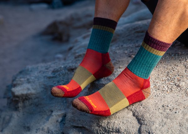 Dos pies apollados en una roca con dos calcetines multicolor rojo, marrón, amrillo y azul