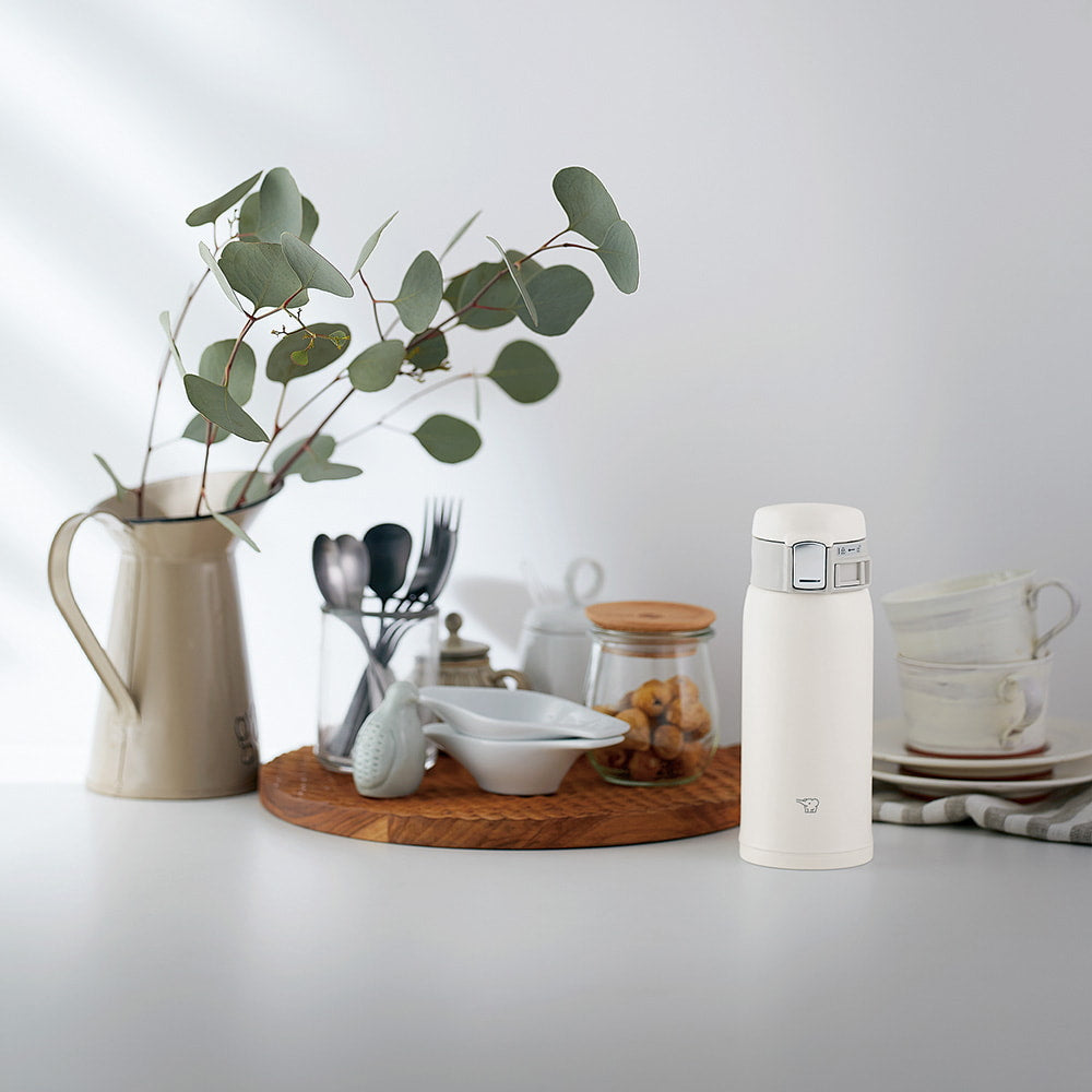 Termo Zojirushi SM-SF color blanco sobre una mesa blanca con elementos decorativos.
