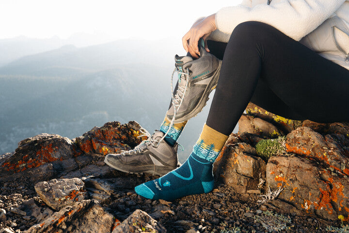 Modelo con calcetines Darn Tough modelo 5013 en una montaña y con botas Merrell en un pie