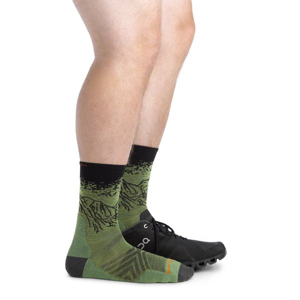 Dos piernas con calcetines verdes con la figura de una montaña en negro a media caña y una con una zapatilla negra.