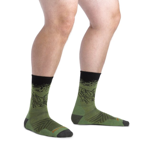 Dos piernas blancas con unos calcetines verdes y negros con la silueta de una montaña