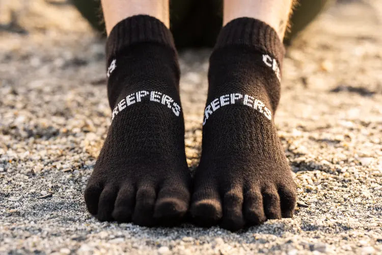 Persona con calcetines negros de dedos en una superficie de grava.