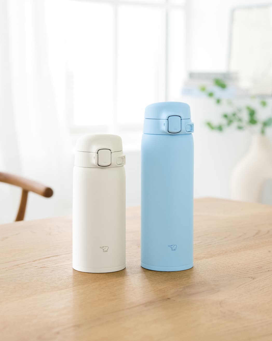 Una botella Azul y otra blanca más pequeña Zojirushi SU-BA sobre mesa de madera y fondo blanco.