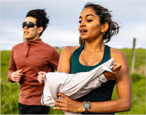 Dos corredores corriendo sobre fondo verde y cielo. La chica se está quitando una chaqueta blanca y el chico con gafas negras corre.